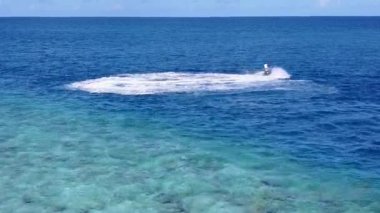 Sahil kenarının geniş açılı doğası mavi denizi aşıp dalgaların yanında temiz kum arkaplanı oluşturur.