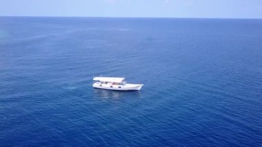 Güzel sahilin güneşli manzarası dalgaların yakınında beyaz kumlu arka planla mavi sulardan kırılıyor.