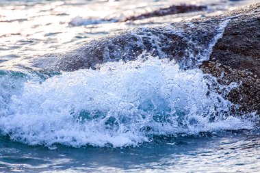 Deniz dalgası bir kaya üzerinde. Gün batımında güneş.