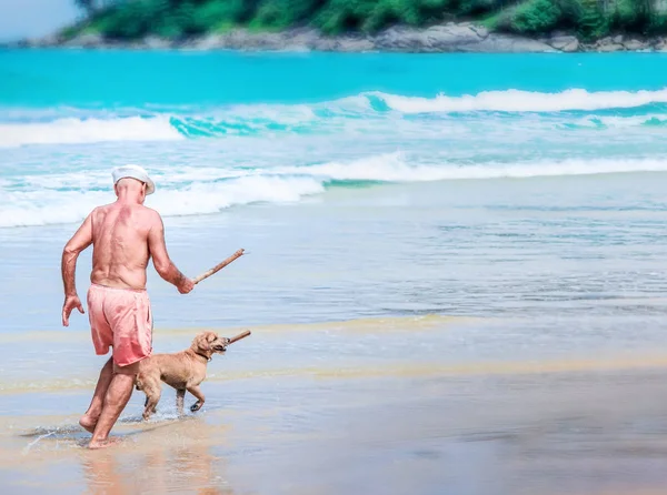 An elderly man runs with a dog on ocean beach.