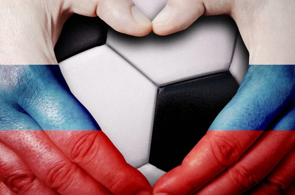 Hands painted with a Russia flag forming a heart over soccer ball background