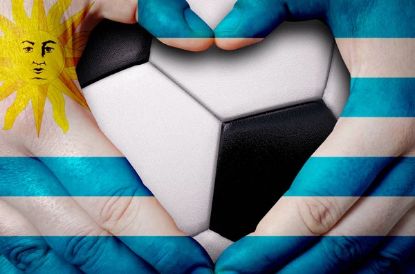 Hands painted with an Uruguay flag forming a heart over soccer ball background