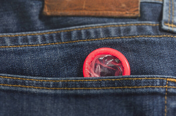 Red condom in the pocket of blue jeans trousers
