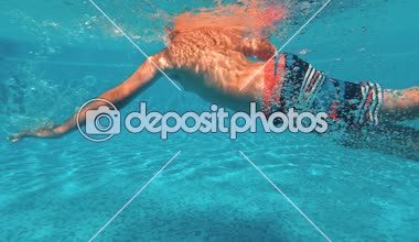 Genç bir adam su altında mavi bir arka plan üzerinde bir yüzme havuzunda yüzüyor. Sualtı video.