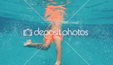 Genç bir adam su altında mavi bir arka plan üzerinde bir yüzme havuzunda yüzüyor. Sualtı video.