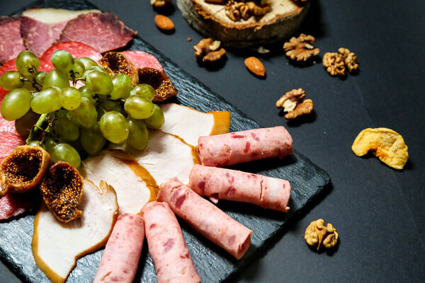 A platter featuring a variety of meats, cheeses, nuts, and grapes arranged artistically.