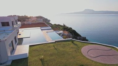 Modern bir villa, günbatımında sakin okyanus ve uzak dağların manzarasını sunan manikürlü bir çimenliğin yanında genişleyen sonsuz bir havuza sahiptir..