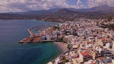 Nefes kesici bir manzara, Girit 'te canlı binaları, hareketli bir marinası ve berrak bir gökyüzünün altında çarpıcı mavi suları olan bir kıyı kasabasını gözler önüne seriyor..