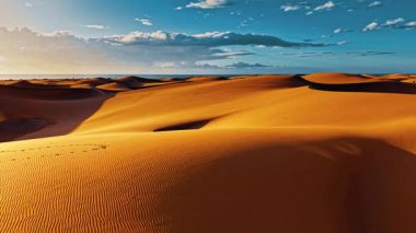 Altın kum tepecikleri İspanya 'nın Gran Canaria bölgesinin her tarafına uzanır. Açık mavi gökyüzü ve dağınık bulutlar altında sıcak güneş ışığıyla aydınlatılır..