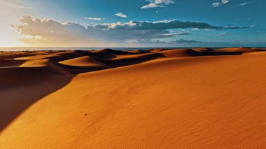Gran Canaria 'nın geniş kum tepelerinin dingin günbatımını keşfedin. Okyanusa karşı çöl manzarasının doğal dalgalanmalarını vurgulayın..