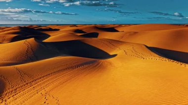 Altın kum tepecikleri, Büyük Kanarya manzarası boyunca uzanır, güneş batarken uzun gölgeler bırakır, gökyüzü ve dünya arasında çarpıcı bir kontrastlık yaratır..