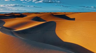 Altın kum tepeleri, gün batımında canlı bir gökyüzünün altında İspanya 'nın Gran Canaria kentindeki manzara boyunca uzanır. Gölgeler yüzeyde büyüleyici desenler yaratır..