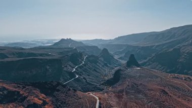 Gran Canaria 'nın dramatik volkanik arazisini, dolambaçlı yolları ve açık mavi gökyüzünün altındaki uzak dağları gösteren nefes kesici hava perspektifi..