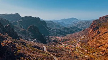 Gran Canaria 'nın çarpıcı hava manzarası açık mavi gökyüzünün altında engebeli dağlar ve vadiler sergiliyor..