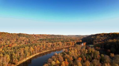 Nefes kesen bir manzara, canlı sonbahar yapraklarıyla çevrili kıvrımlı bir nehri yakalar ve berrak mavi gökyüzünün altında, doğanın sıcacık renklerinde güzelliğini gösterir..