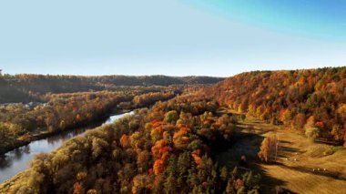 Canlı sonbahar ağaçları akan bir nehrin çevresini sarar ve resim gibi bir manzara yaratır. Vadiler ve tepeler sıcak renklerle süslenir, mevsimin güzelliğini gözler önüne serer..