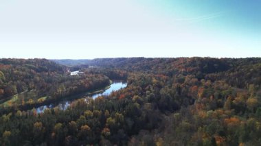 Renkli ağaçlar, huzurlu bir kırsal alanda dolambaçlı bir nehrin etrafında canlı sonbahar yaprakları sergiliyor. Güneş dingin sahnenin üzerine ılık bir parıltı saçar..