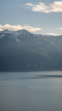 Geniş Geneva Gölü manzaralı küçük bir tekne, Fransız ve İsviçre Alpleri ile çevrili çoğunlukla açık bir gökyüzü altında.