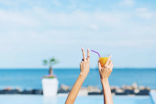 Picture of hands of girl holding cocktail on the sea background. It looks cool