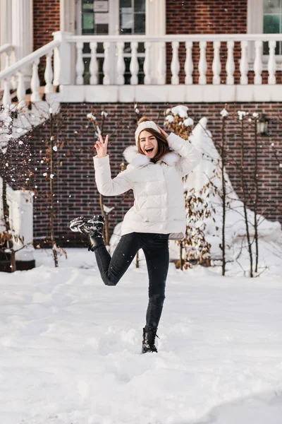 Brightful true emotions of excited stylish woman having fun in snow on street in cold winter time. Smiling, jumping, knitted hat, warm clothes, cheerful mood, winter holidays, god mood.