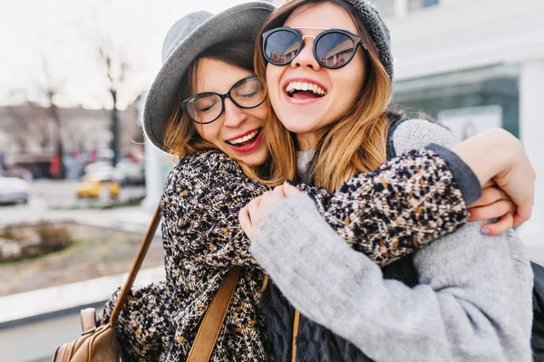 Happy brightful positive moments of two stylish girls hugging on street in city. Closeup portrait funny joyful attarctive young women having fun, smiling, lovely moments, best friends.