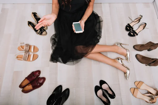 Woman sitting on floor surrounded a lot of shoes.