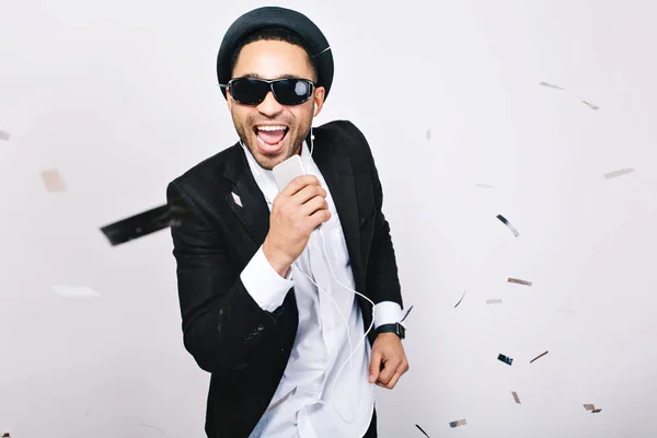 Entertainment, celebrating karaoke party of excited handsome guy in black sunglasses having fun on white background. Fashionable look, singing, music, enjoying, expressing positivity, happiness.