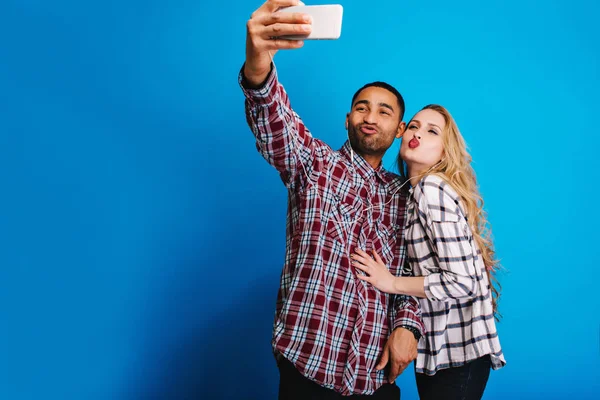 Happy moments of funny couple making selfie portrait on blue background. Having fun, stylish, fashionable outlook, young attractive blonde woman, relaxing, weekends. Place for text.