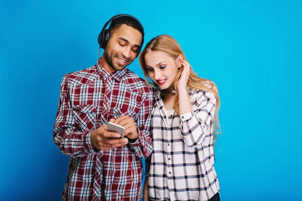 Enjoying free time of cute couple young stylish handsome man and woman having fun tohgether on blue background. Listening to music, weekends, relaxing, songs, modern.