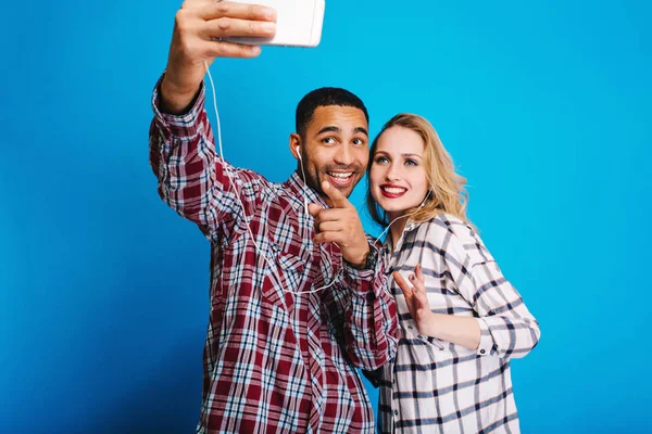 Joyful handsome guy making selfie portrait with pretty young blonde woman on blue background. Having fun, fashionable outlook, cheerful mood, smiling, relaxing, free time, weekends.