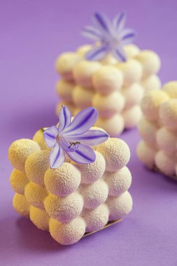 Beyaz çikolata kadifesiyle kaplanmış, çiçeklerle süslenmiş küçük kremalı kekler.