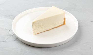 Beton bir zeminde beyaz bir tabakta ev yapımı peynirli kek.