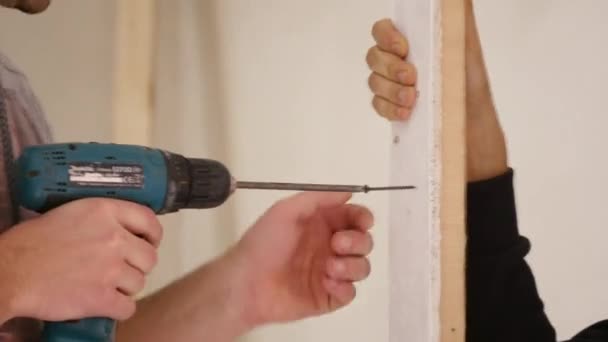 Рабочий прикрепляет доску к стене с помощью электрической отвертки — стоковое видео