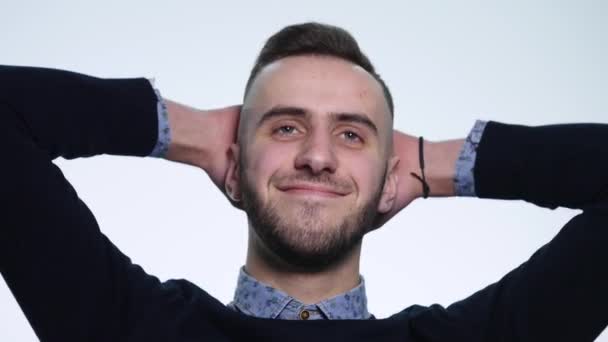 Glücklich schöner junger Mann lächelt und legt seine Hände hinter seinen Kopf, isoliert auf weißem Hintergrund — Stockvideo