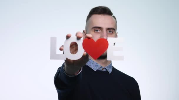 Een jonge man houdt de inscriptie liefde op witte achtergrond — Stockvideo