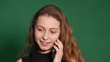 Genç kadın gülümseyerek ve beyaz zemin üzerine onu cep telefonuyla konuşuyor. Telefon ve görünüyor uzakta yeşil zemin üzerine konuşan bir genç casual kadın önden görünümü.