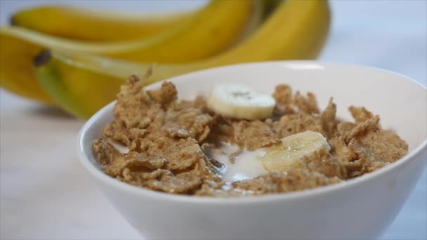 Corn flakes s mlékem jsou v misce. kousky banánů klesnout na vrcholu této lahodné snídaně. Close-up shot — Stock video