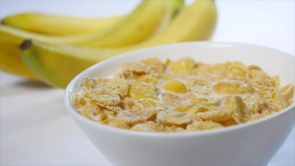 Los copos de maíz con leche están en un tazón. trozos de banana caen en la parte superior de este delicioso desayuno. Primer plano de disparo — Vídeos de Stock