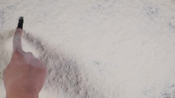 Écrivez un doigt FLUX sur un fond de farine blanche. vue du dessus 4k 