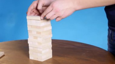 eller genç adam çalış jenga üzerinde mavi arka plan, yakın çekim. Bir adam bir kule bloklar jenga oynarken oluşturur