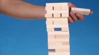 eller genç adam çalış jenga üzerinde mavi arka plan, yakın çekim. Bir adam bir kule bloklar jenga oynarken oluşturur