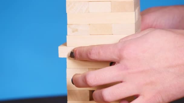 Kvinnans händer spelar brädspelet Jenga. blå bakgrund — Stockvideo