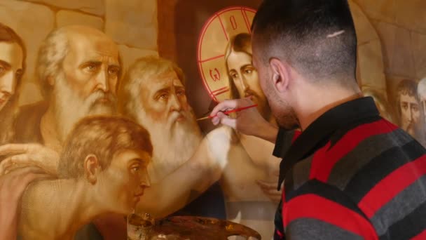 Artista Masculino está de pé e pintando o Ícone do Santo Ortodoxo, segurando uma paleta com tintas — Vídeo de Stock