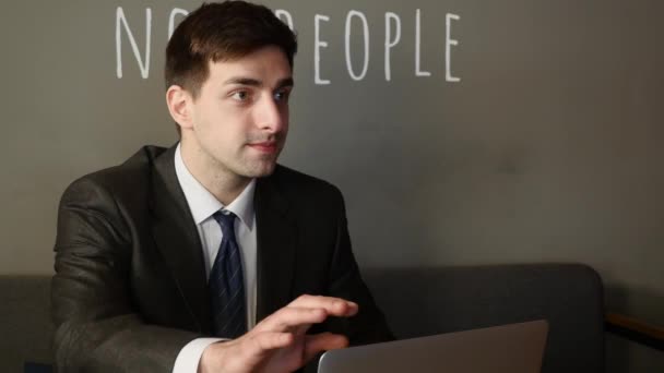 Joven hombre de negocios trabajando en el ordenador portátil y hablando con el cliente, en la mesa en la cafetería — Vídeos de Stock