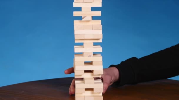 Handen van de jonge mens speelt jenga op blauwe achtergrond, close-up. Een man bouwt een toren van blokken terwijl het spelen van jenga — Stockvideo