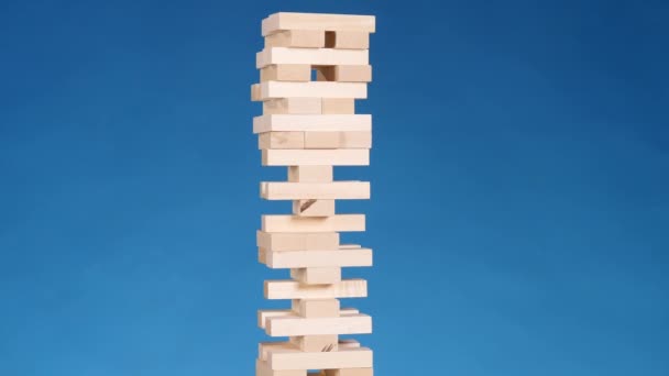 Manos de Joven juega jenga sobre fondo azul, de cerca. Un hombre construye una torre de bloques mientras juega jenga — Vídeo de stock