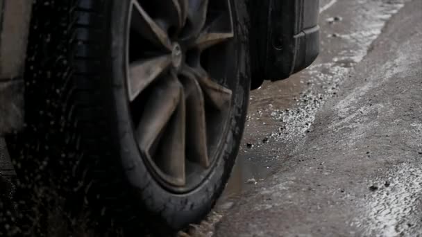 MOTION LENT, FERMER : L'eau trouble éclabousse la route asphaltée alors que la voiture roule dans la flaque d'eau. Sprays liquides marron à travers la rue noire — Video