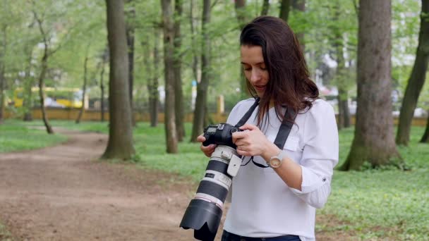 Молода жінка-фотограф робочий процес зйомки на відкритому повітрі в парковій природі — стокове відео