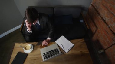 İşadamı smartphone kafede üzerinde görüşmeler ve iş kağıtları ile çalışır. Adam kafede masada oturur ve cep telefonuyla, tablo üzerinde dizüstü yalan konuşuyor. üstten görünüm