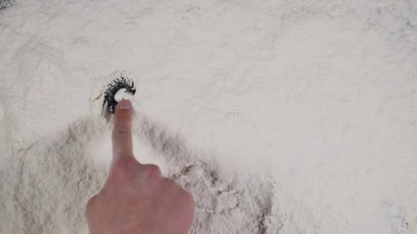 Палець малює смішну усмішку на білому фоні борошна. вид зверху 4k — стокове відео